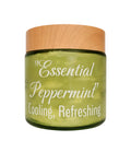 A green glass jar with a light wood lid, labeled 'Essential Peppermint Cooling, Refreshing' in white script, on a plain white background.